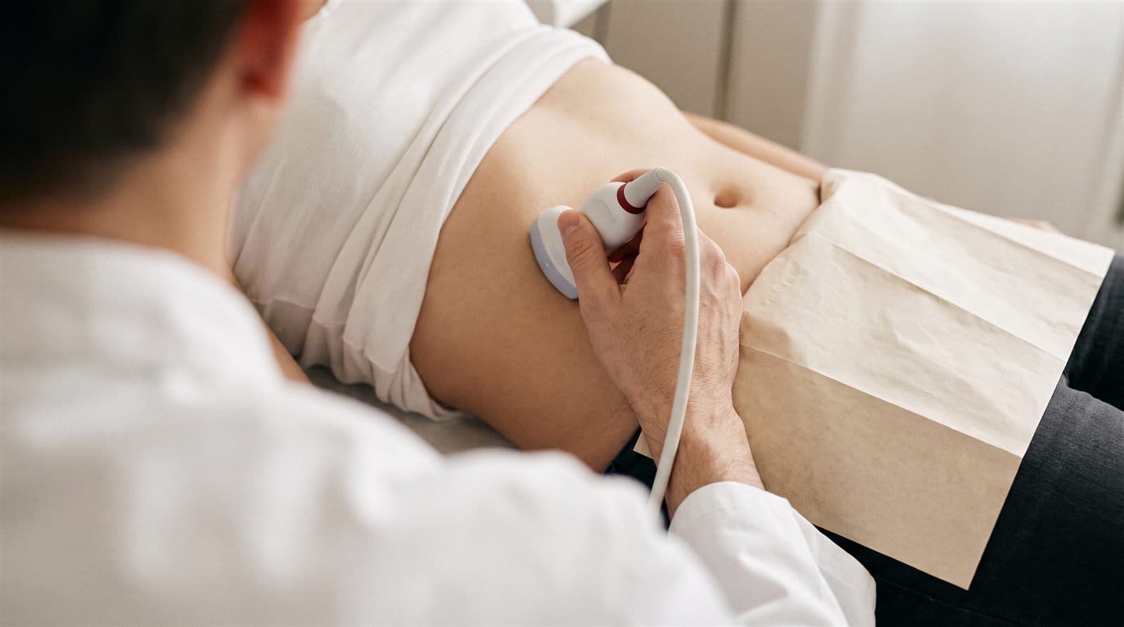 Bauch-Ultraschalluntersuchung in einer Hausarztpraxis, Nahaufnahme von Schallkopf und Hand